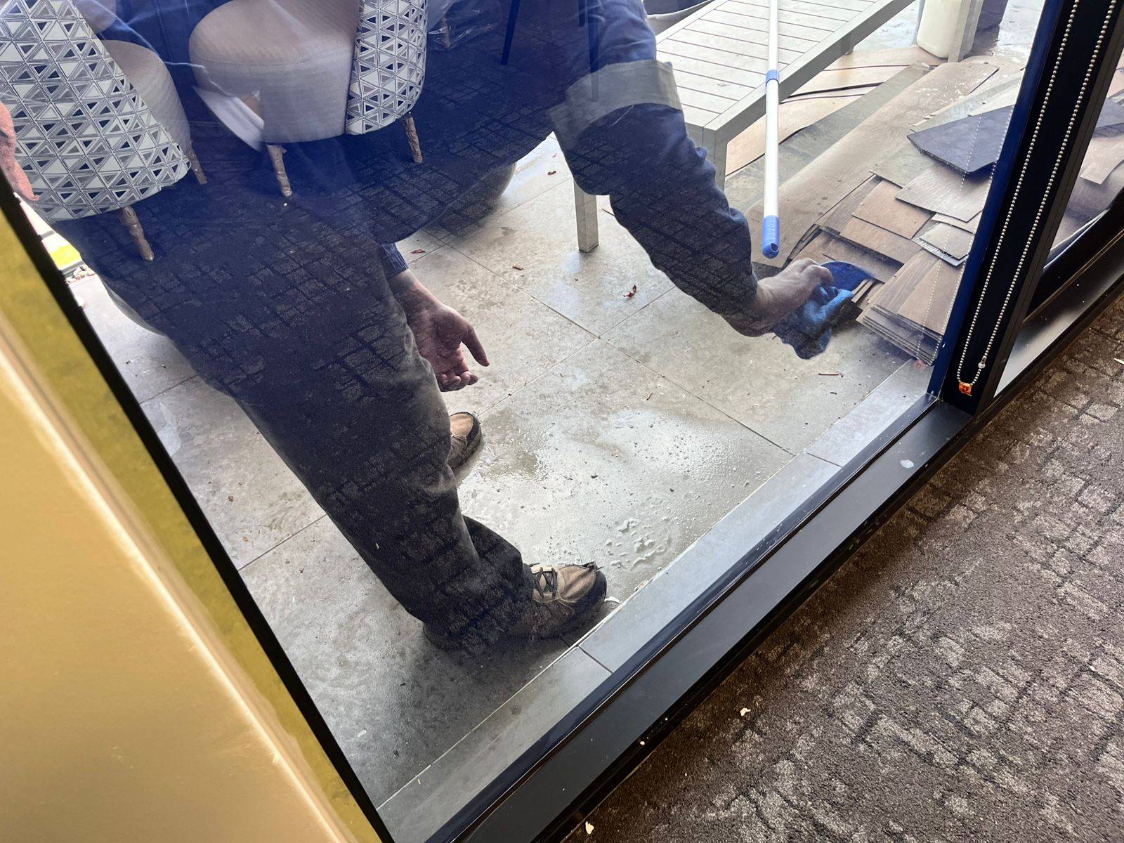 Worker's boots and cleaning equipment near a glass door track